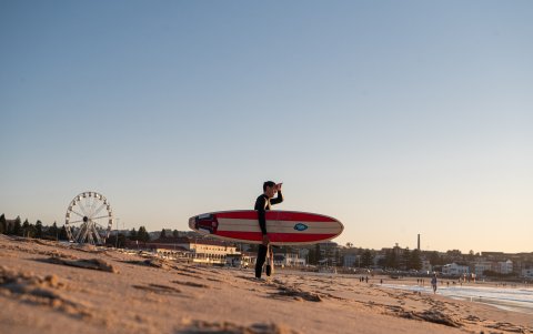 Panorama. Un surfista atraviesa una playa australiana, en una tarde muy soleada.