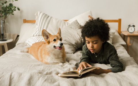 Un niño lee mientras aparece acompañado por su perro. La convivencia con su mascota, ayuda al menor.