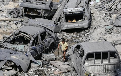 Un niño palestino pasa junto a coches dañados en medio de los escombros de una zona destruida tras los ataques aéreos israelíes en la ciudad de Gaza, este lunes.