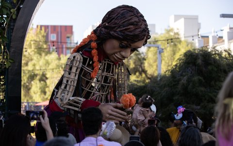 La gente se reúne y rodea a Little Amal mientras camina por el Monumento Histórico El Pueblo de Los Ángeles.