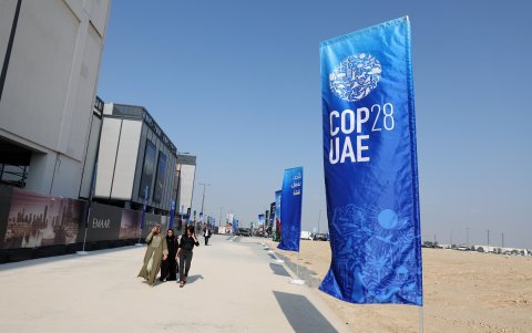 Un grupo de personas caminan en una área de Dubai donde se observa una pancarta con el logotipo de la COP28.