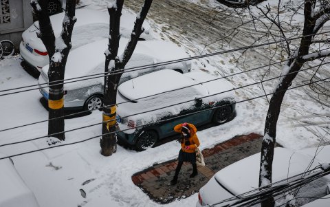 Una mujer camina por una acerca entre carros cubiertos por la nieve.
