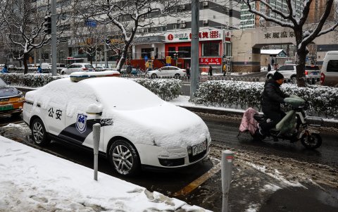 Un hombre pasa en una scooter eléctrica cerca de un coche de policía que está cubierto de nieve en Pekín.