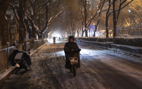 Un motociclista transita por una avenida con un gruesa capa de nieve.