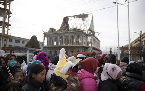 Las mujeres esperan en fila para conseguir comida, con una mezquita dañada por el terremoto al fondo, en un campamento para personas desplazadas por el terremoto, en Dahejia, provincia de Gansu.