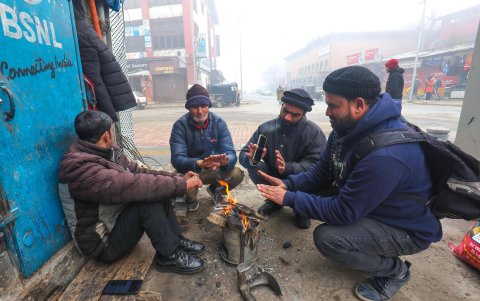 La gente se calienta cerca de un pequeño fuego en una mañana fría y brumosa en Srinagar, Cachemira, India, 27 de diciembre de 2023.