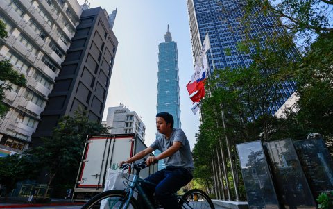 Un ciclista circula junto a una bandera de Taiwán en una calle desde la que se ve el rascacielos Taipei 101, el 12 de enero de 2024, un día antes de las elecciones presidenciales.