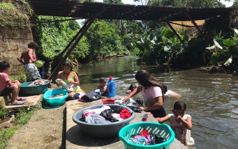 Trabajo. Un par de mujeres lava ropa ajena, como trabajo, mientras sus hijos se divierten en el agua.