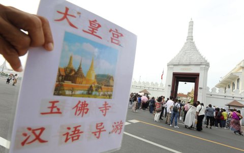 Turistas chinos y otras personas esperan para visitar el Templo del Buda Esmeralda dentro del Gran Palacio, junto a un cartel de guía turístico escrito en chino, en Bangkok.
