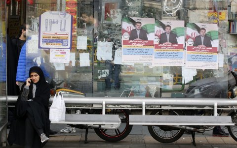 Una mujer iraní con velo se sienta en una estación de autobuses junto a carteles de campaña electoral de candidatos parlamentarios