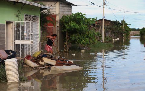 Una mujer procura aglomerar los enseres destruidos en medio del agua que rodea su casa en Playas.
