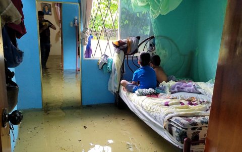 Niños permanecen sobre una cama dentro de una casa totalmente anegada tras las lluvias y crecientes de los ríos en el sector de El Palmar, zona rural de Babaoyo.