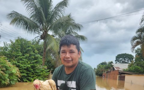 Un joven mientras carga un gallo tras ser rescatado de una inundación