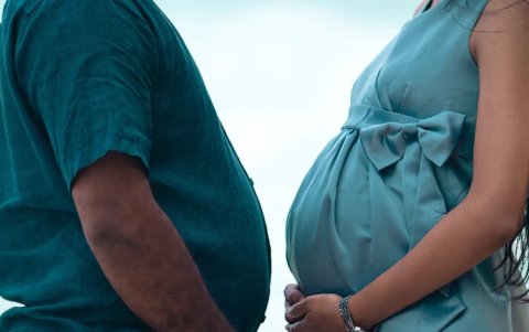 Hombre con sobrepeso y mujer embarazada, frente a frente, sosteniendo sus vientres con sus manos.