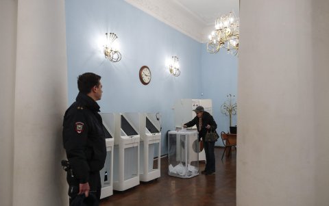 Una mujer vota en un colegio de Moscú mientras un policía brinda seguridad al lugar.