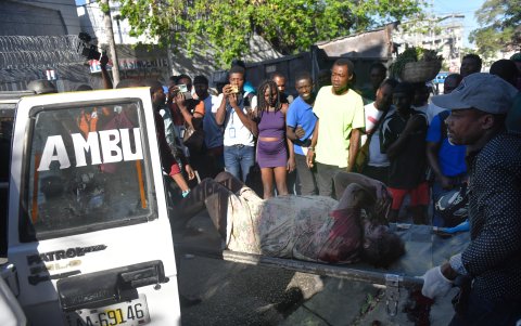 Dos hombres levantan del suelo el cadáver de una persona este 18 de marzo, en Puerto Príncipe