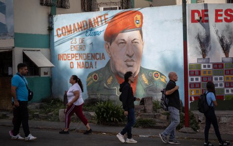 Varias personas caminan frente a un mural del fallecido presidente venezolano Hugo Chávez