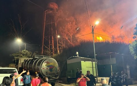 Uno de los incendios forestales en los alrededores de Caracas, se desarrolla, mientras varias personas observan desde lejos.