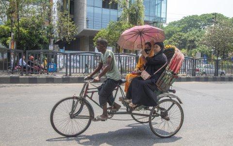 Una familia se traslada en uno de los triciclos que ofrecen servicio de traslados por un calle de la capital Daca.
