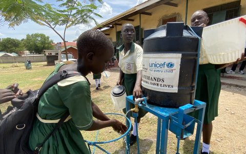 Un profesor carga el bidón de agua limpia mientras una alumna se lava las manos antes de comer su ración correspondiente aportada por el PMA para la escuela Al Salam B Primary School de Yuba.
