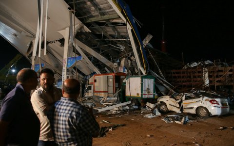 Personas observan los daños en una gasolinera en la India después de que cayera sobre ella una valla publicitaria.