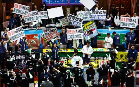 Los legisladores sostienen pancartas y cantan para interceptar aviones de papel liberados por los legisladores del Partido Democrático Progresista.