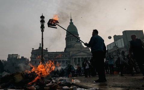 Un hombre quema una caja durante enfrentamientos entre la policía y personas que protestan a las afueras del senado durante un debate este miércoles, en Buenos Aires (Argentina).