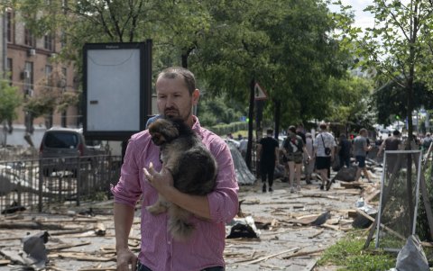 Un hombre sostiene un perro camina por una calle cubierta de escombros después de un ataque con misiles en Kiev, Ucrania, el 8 de julio de 2024.