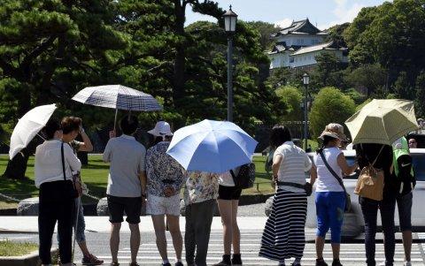 Varias personas se protegen del sol mientras pasean por los jardines del Palacio Imperial en Tokio.