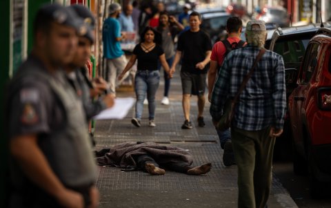 Una persona duerme en medio de un pasaje comercial entre vendedores, policías y compradores, en una ciudad de Brasil.