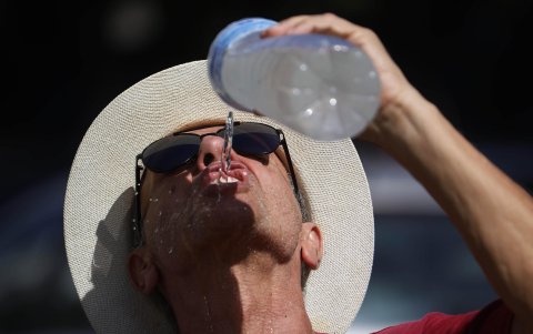 Un hombre se refresca con agua de una botella mientras camina por el Puente Romano de Córdoba.