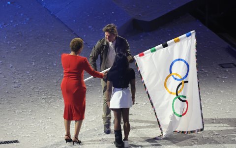 La alcaldesa de Los Angeles, Karen Bass (i), y la gimnasta Simone Biles, entregan la bandera olímpica actor estadounidense Tom Cruise