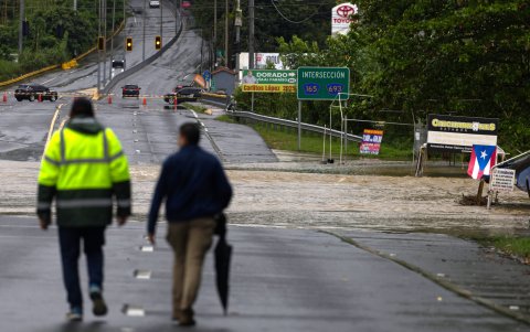 Dos personas caminan por una carretera que está cortada al tráfico por el desbordamiento de un río.