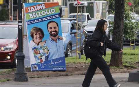 Una mujer camina frente a un afiche con propaganda electoral