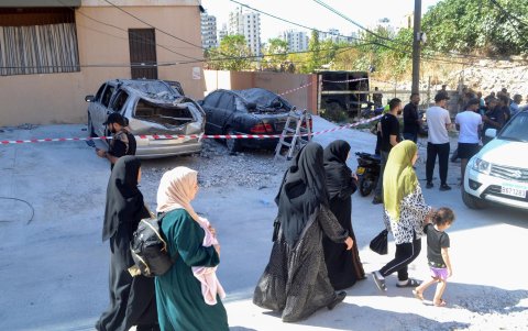 La gente pasa junto a coches dañados en el lugar donde un edificio de apartamentos fue atacado por un ataque militar israelí en el campo de refugiados palestinos de Beddawi.
