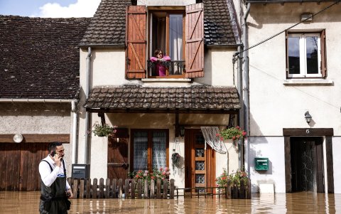 Una mujer observa desde su balcón cómo un oficial de policía local avanza a través de las aguas de la inundación frente a su casa en Tresmes, Francia.
