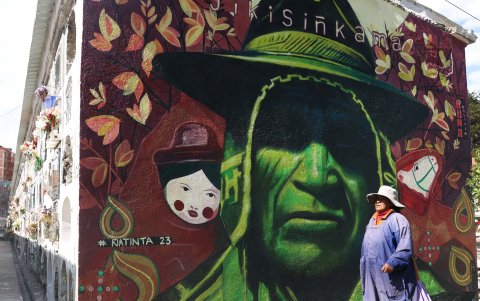 Una mujer aimara camina delante de un mural perteneciente al proyecto 'Ñatinta', en los pasillos del cementerio general, en La Paz (Bolivia).