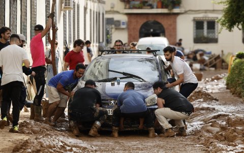 Un grupo de personas se ocupan en retirar un vehículo atrapado entre el lodo, en el barrio de La Torre, en Valencia, este viernes.