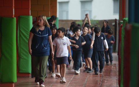 Un grupo de niños se encaminan a una de sus aulas acompañados de una de sus profesoras.
