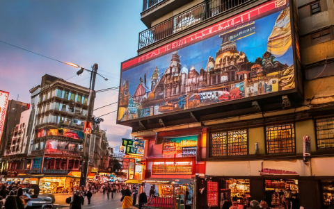 La imagen muestra una avenida animada, con edificios decorados por coloridas pantallas electrónicas y luces brillantes que capturan la atención.