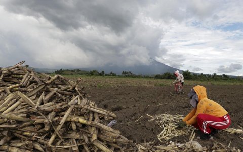 Agricultores trabajan en un campo de caña de azúcar mientras se ve al fondo el volcán Monte Kanlaon, un día después de su explosiva erupción, en la ciudad de La Castellana, centro de Filipinas.