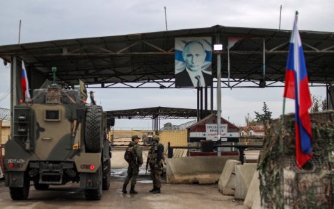 Un retrato de Vladimir Putin, cuelga arriba mientras camiones militares rusos ingresan a la base militar siria arrendada por Rusia de Hmeimim, en el oeste de Siria