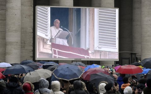 Fieles se reúnen cerca de una pantalla que muestra al Papa Francisco dirigiendo su oración del Ángelus.