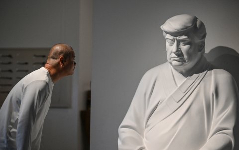 Hong Jinshi junto a una escultura de Donald Trump, en una pose que evoca a Buda.