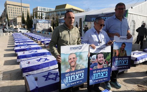 Familiares de soldados israelíes caídos se encuentran cerca de una exhibición de ataúdes simulados envueltos en banderas israelíes durante una protesta contra un acuerdo de alto el fuego.