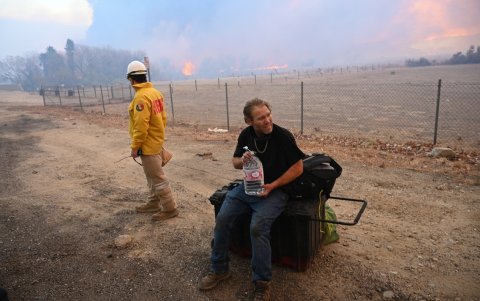 Un hombre que salió de la zona del incendio recibe agua mientras la columna de humo del incendio de Hughes llena el cielo en Castaic, el 22 de enero de 2025.