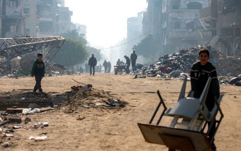Un niño empuja un carrito cargado con muebles de jardín cerca de montículos de escombros y basura a lo largo de una calle de la ciudad de Gaza el 27 de enero de 2025.