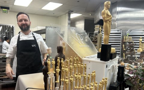 Un ayudante de cocina posa junto a figuras de chocolate de la estatuilla de los premios, que serán parte de la cena.