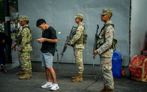 Un hombre mira su celular mientras integrantes de las Fuerzas Armadas de Perú custodian las calles este martes, en Lima (Perú).