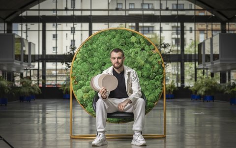 Valentyn Frechka sentado, con un panel de materia vegetal a sus espaldas.